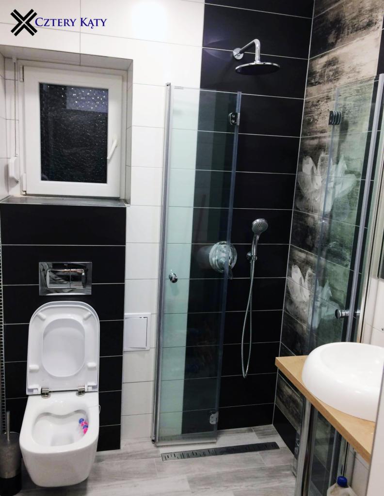 Nowoczesna łazienka z czarno-białymi płytkami, kabiną prysznicową typu walk-in, podwieszaną toaletą z otwartą klapą i umywalką nablatową na drewnianym blacie.
