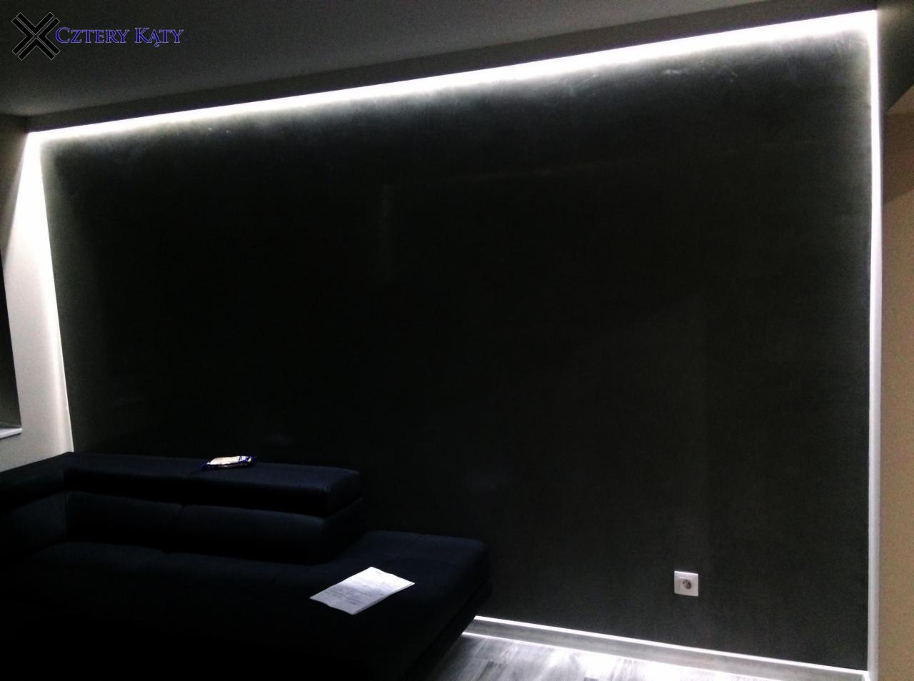 Ciemna ściana z efektem dekoracyjnym oświetlona listwą LED, widoczny fragment czarnego narożnika i szara podłoga.