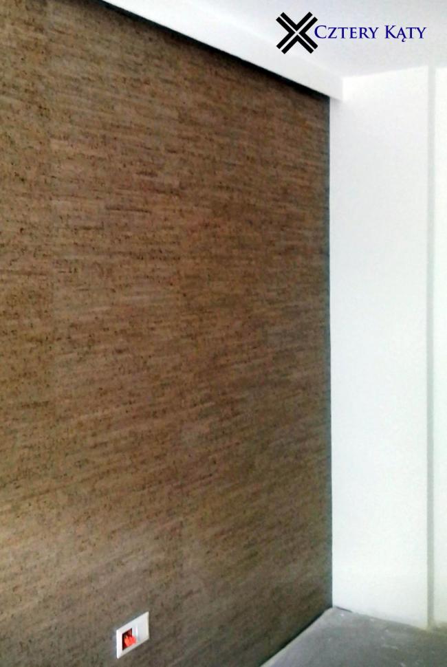 Brązowa ściana z wyraźną fakturą, narożnik pomalowany na biało, widoczny włącznik światła i logo firmy 'Cztery Kąty' na górze ściany.