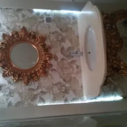 Umywalka z dekoracyjną, złoconą podstawą i ozdobne lustro w złotej ramie na ścianie z wzorzystymi płytkami w wyremontowanej łazience.