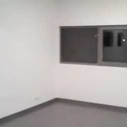 Pusty, pomalowany na biało pokój z szarymi oknami i podłogą, widoczne odbicia świateł w szybach.