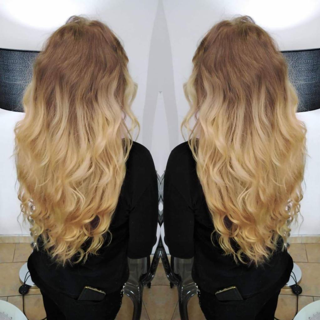 Długie, falowane włosy z ombre w odcieniach brązu i blondu, widok z tyłu, wykonane w salonie z jasnym tłem.