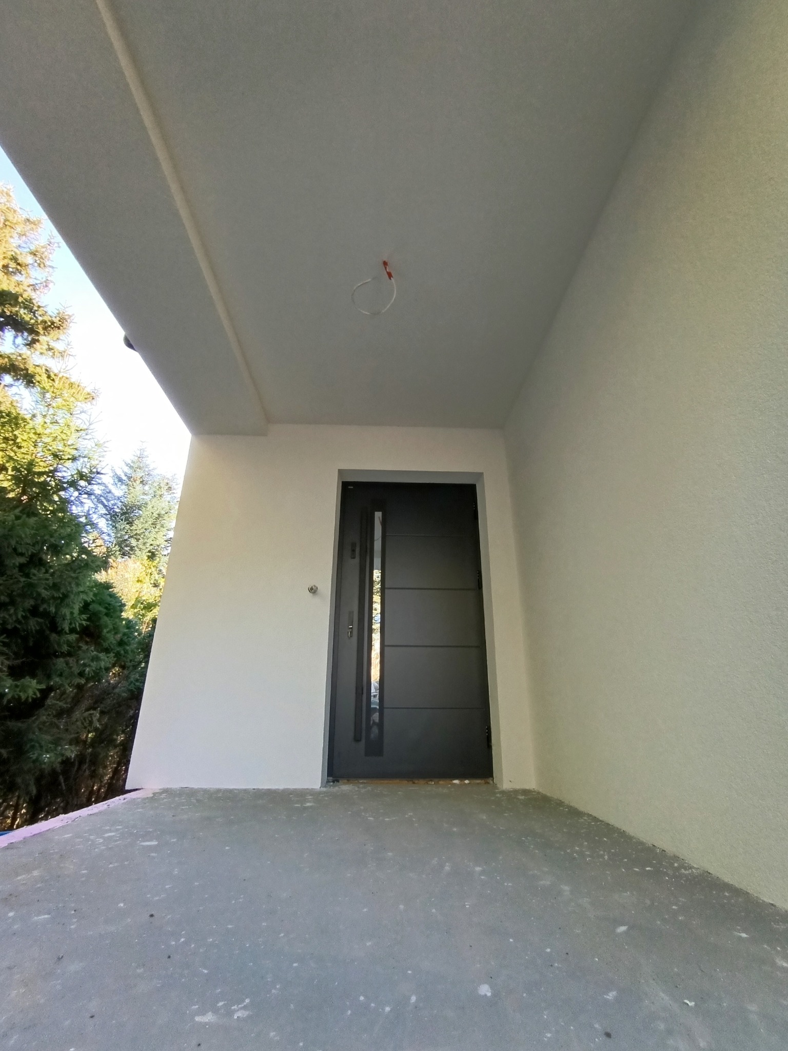 Nowoczesne wejście do domu z szarą elewacją, ciemnymi drzwiami z przeszkleniami i betonową podłogą, widok z dołu.