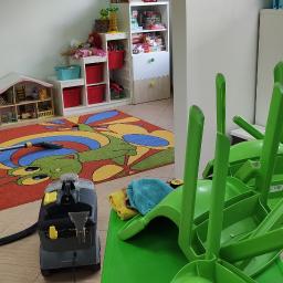 Firma sprzątająca Efekt - Profesjonalny odkurzacz piorący Kärcher na tle dywanu z motywem smoka w pokoju dziecięcym, zielone krzesła ustawione na stole, w tle regał z zabawkami i komoda.