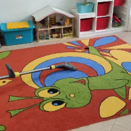 Czyszczenie kolorowego dywanu z motywem zwierzęcym w Zawierciu za pomocą odkurzacza piorącego. W tle widoczne zabawki i meble dziecięce.