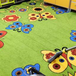 Firma sprzątająca Efekt - Profesjonalny odkurzacz piorący czyści zielony dywan dziecięcy z motywem kwiatów i motyli w pokoju zabaw.