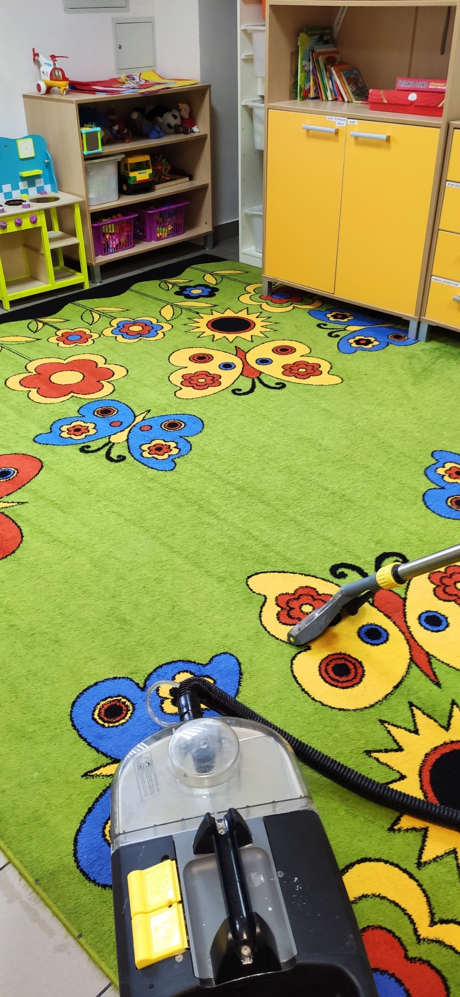 Profesjonalny odkurzacz piorący czyści zielony dywan dziecięcy z motywem kwiatów i motyli w pokoju zabaw.