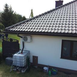 Lalsystem - Biały dom w Młochowie z klimatyzatorem na ścianie, zbiornikiem na deszczówkę i ciemną dachówką. W tle widoczni trzej mężczyźni na trawniku.