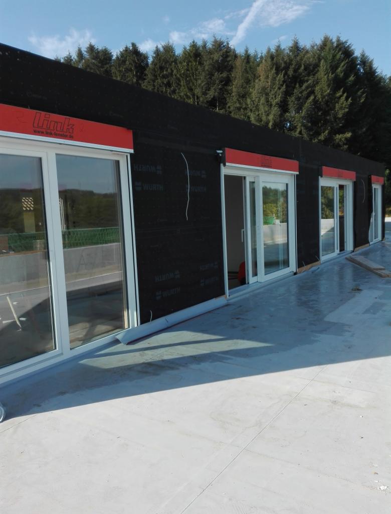 Montaż okien z roletami zewnętrznymi w budynku z czarną membraną, widoczne logo Link i Wurth na folii izolacyjnej.