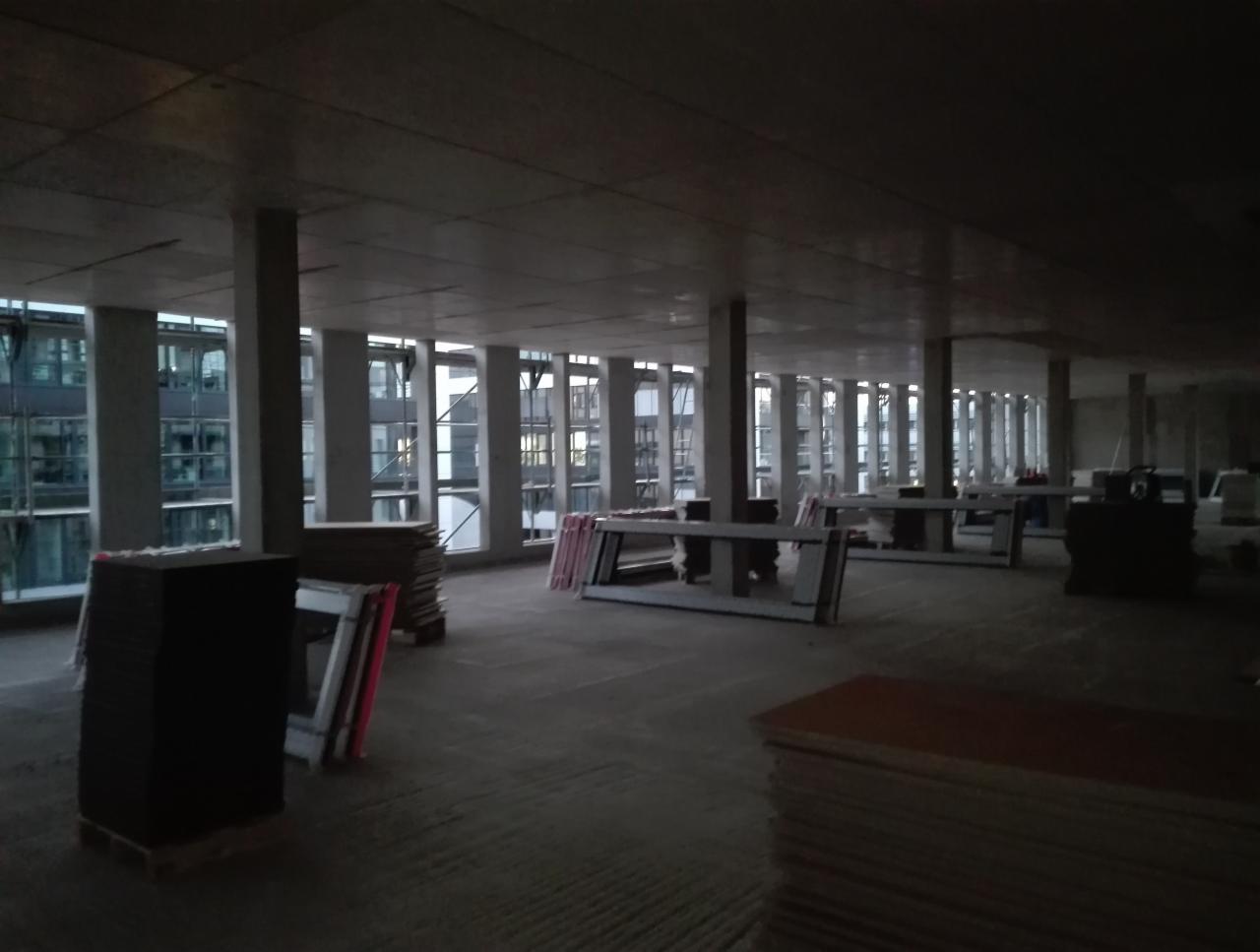 Wnętrze w stanie surowym z rzędami okien, stosami płyt i ram okiennych przygotowanych do montażu.