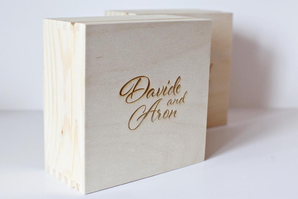 Dwie jasne, drewniane skrzynki z wygrawerowanym laserowo napisem 'Davide and Aron' na froncie, widoczne połączenia na rogach.
