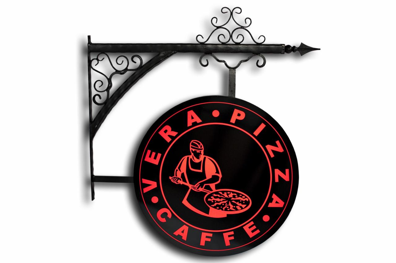 Okrągły szyld z kutego żelaza, czarne tło z neonowo-czerwonym napisem 'VERA PIZZA CAFFE' i grafiką kucharza przygotowującego pizzę.