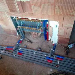 Rozdzielacz ogrzewania podłogowego wnęce z cegły, rury izolowane pianką PUR, pistolet do pianki w tle.