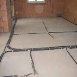 Rozprowadzenie przewodów elektrycznych w peszlach, przytwierdzonych do surowej podłogi w nowo budowanym domu z cegły.