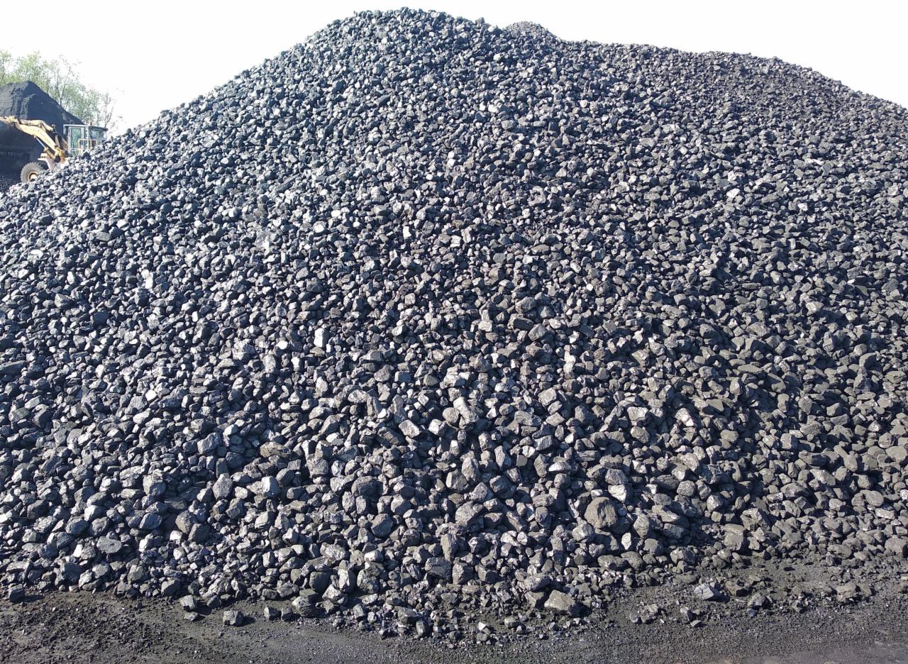 Ogromny pryzmat czarnego węgla kamiennego w składzie, z widoczną koparką w tle po lewej stronie.