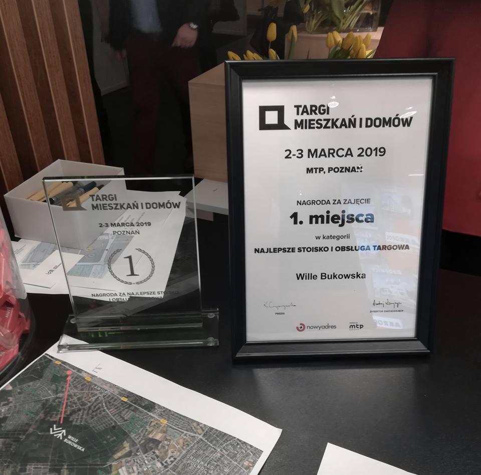 Dyplom i statuetka za zajęcie 1. miejsca na Targach Mieszkań i Domów w Poznaniu za najlepsze stoisko i obsługę targową, obok mapa z zaznaczoną lokalizacją firmy Wille Bukowska.