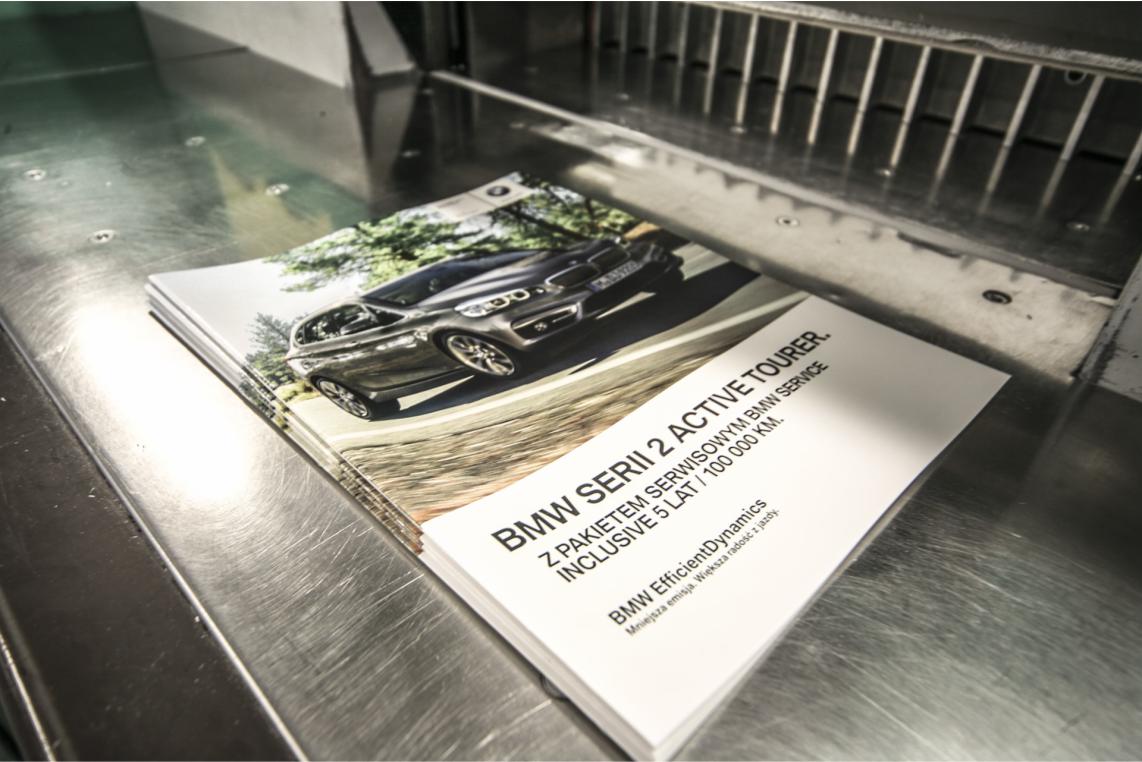 Stos drukowanych katalogów BMW Serii 2 Active Tourer pod nożem gilotyny introligatorskiej, gotowych do pocięcia.