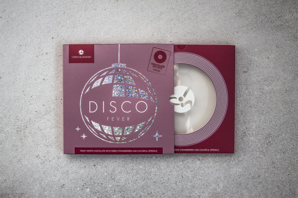 Pudełko czekoladek Chocolissimo Disco Fever z grafiką kuli dyskotekowej i motywem płyty winylowej, leżące na szarym tle.