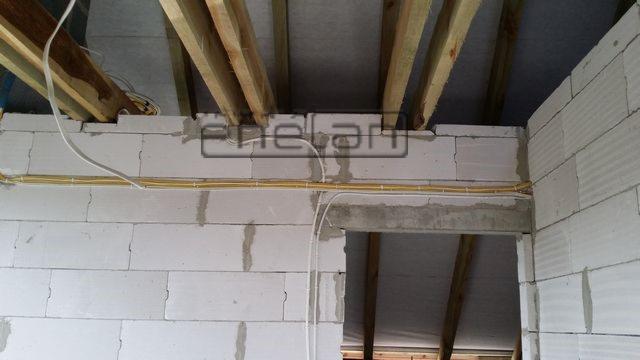 Ściana z betonu komórkowego z widocznymi kablami elektrycznymi w peszlu i drewnianą konstrukcją stropu podczas montażu instalacji.