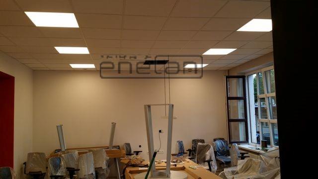 Białe panele LED w suficie podwieszanym biura, widoczne instalacje elektryczne i wiszące kable, przygotowanie do montażu oświetlenia.