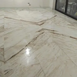 Beżowa podłoga z marmuru ułożona we wzór rombów, widok na ścianę z gniazdkami i duże okno przesuwne.