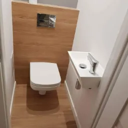 Nowoczesna, minimalistyczna toaleta w Czarnym Dunajcu z drewnopodobnymi panelami ściennymi i podłogą, podwieszana miska WC, umywalka nablatowa z chromowaną baterią oraz ukryta spłuczka.