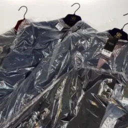 Trzy garnitury męskie w pokrowcach foliowych wiszące na wieszakach, widoczne metki sklepu Next.