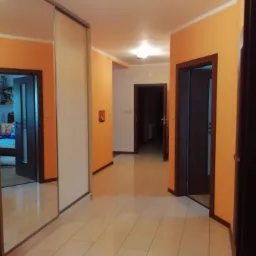 Korytarz w mieszkaniu po remoncie, pomarańczowe ściany, jasne płytki podłogowe, ciemne drzwi z ościeżnicami, lustrzana szafa w zabudowie po lewej stronie.