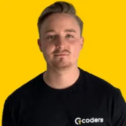 Portret młodego mężczyzny z krótką fryzurą i lekkim zarostem, ubranego w czarną koszulkę z logo 'Gcoders' na żółtym tle.