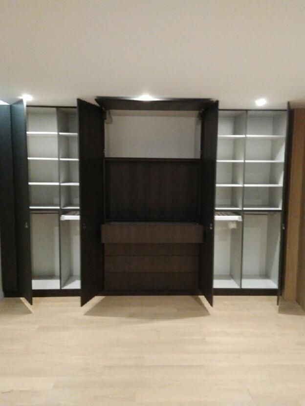 Przestronna szafa wnękowa z otwartymi drzwiami, ukazująca półki i szuflady wewnątrz, oświetlona punktowymi lampami sufitowymi, na jasnej drewnianej podłodze.