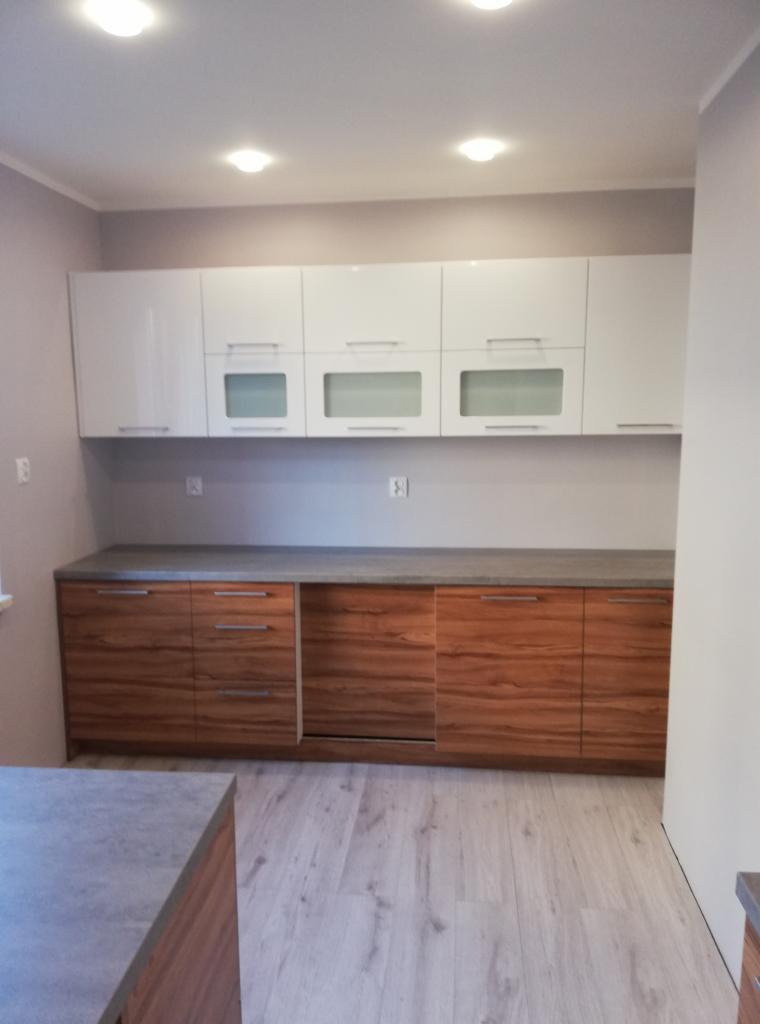 Nowoczesna kuchnia z białymi szafkami górnymi z przeszklonymi frontami i drewnopodobnymi szafkami dolnymi z szarym blatem.