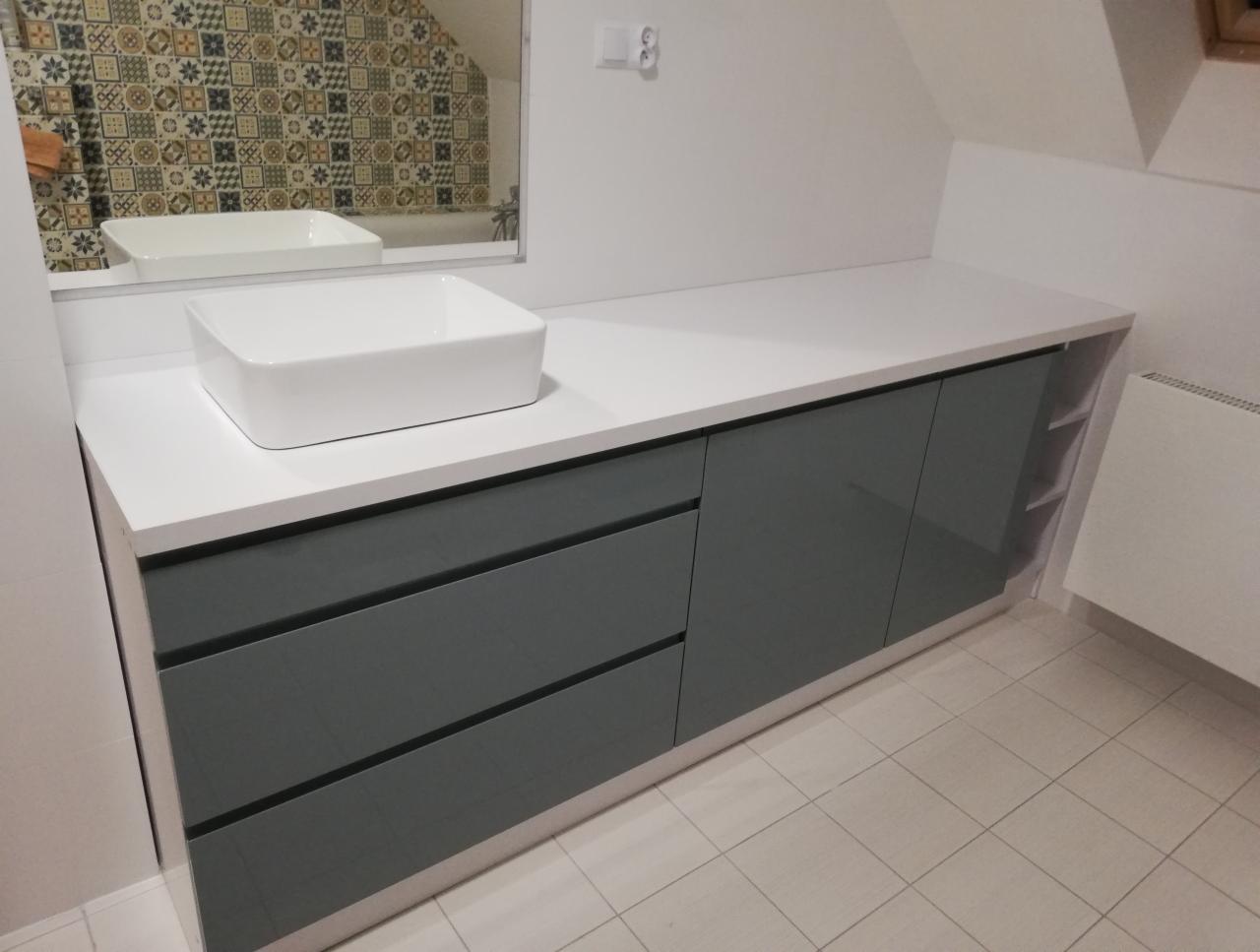 Nowoczesna łazienka z szarymi szafkami pod umywalką nablatową i blatem z białego konglomeratu, widoczne płytki w stylu patchwork w lustrze.