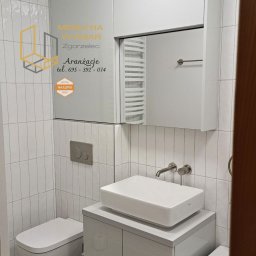 ABT Service Meble - Nowoczesna łazienka z białymi meblami na wymiar: szafka pod umywalkę z półką, szafka wisząca z lustrem, biała armatura, płytki wertykalne i podłoga lastryko. Na lustrze naklejka z logo firmy.