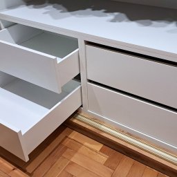 ABT Service Meble - Biała szafa wnękowa z otwartymi szufladami, widoczne złote akcenty na prowadnicach i obramowaniu, parkiet na podłodze. Szuflady z pełnym wysuwem.