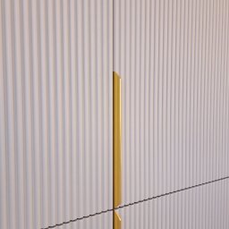 ABT Service Meble - Biała szafa z ryflowanymi frontami i złotymi uchwytami, widok z bliska, prezentująca nowoczesny design i dbałość o detale.