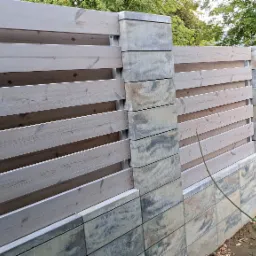 Nowoczesne ogrodzenie z poziomych, lakierowanych desek w odcieniach szarości, osadzone na słupkach z szarej, warstwowej kostki betonowej.