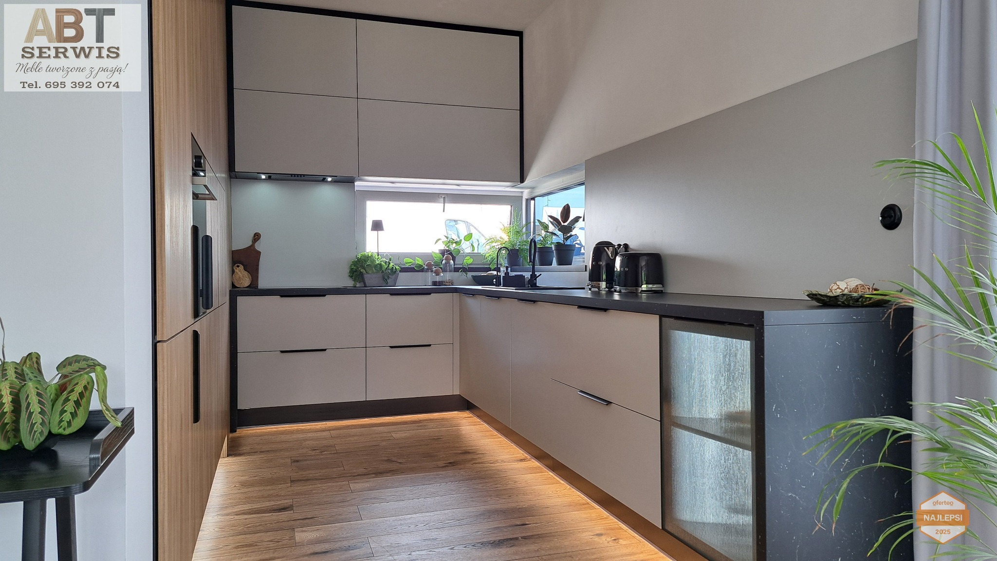 Nowoczesna kuchnia w Zgorzelcu z drewnianą podłogą i minimalistycznymi frontami. Blat w kolorze czarnym, okno z roślinami. Oświetlenie LED pod szafkami.