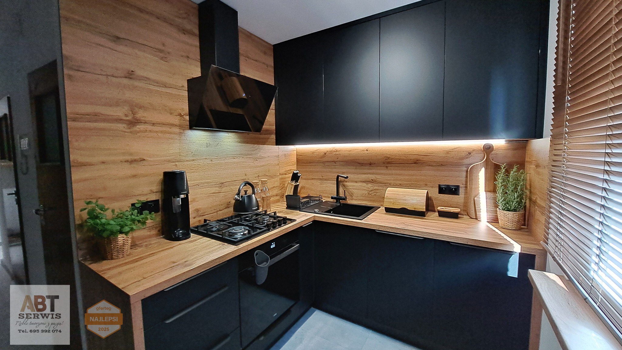 Nowoczesna, czarna kuchnia z drewnianymi elementami, oświetleniem LED i akcesoriami. Widok na narożną zabudowę z blatem i okapem.