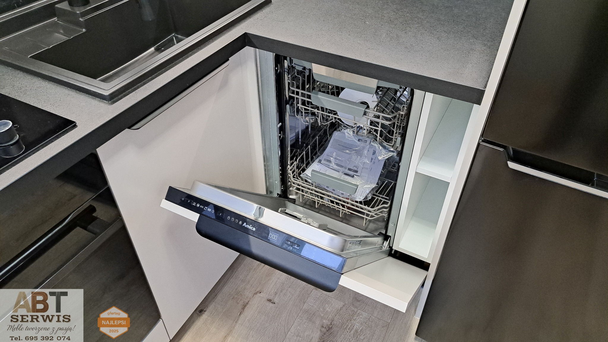 Nowoczesna kuchnia z szarym blatem i otwartą zmywarką Amica, w której widać instrukcję obsługi. Minimalistyczny design, drewniana podłoga.