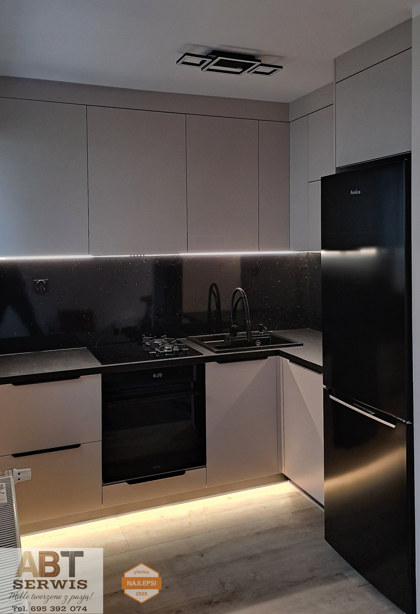 Nowoczesna kuchnia z szarymi frontami, czarnym blatem i sprzętem Amica. Oświetlenie LED podkreśla minimalistyczny design. Widoczny fragment płyty gazowej i zlewozmywaka.