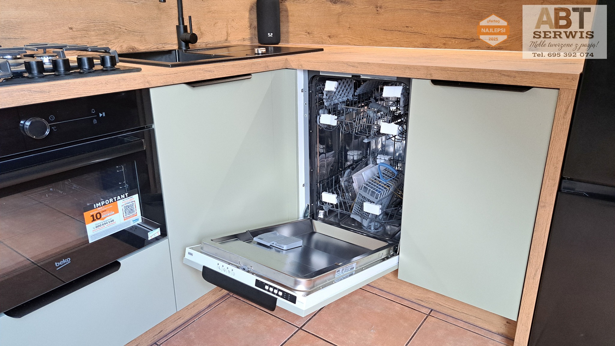 Kuchnia na wymiar z otwartą zmywarką w zabudowie. Fronty w odcieniach szarości, drewniany blat i brązowa podłoga. Widoczny piekarnik Beko i płyta gazowa.