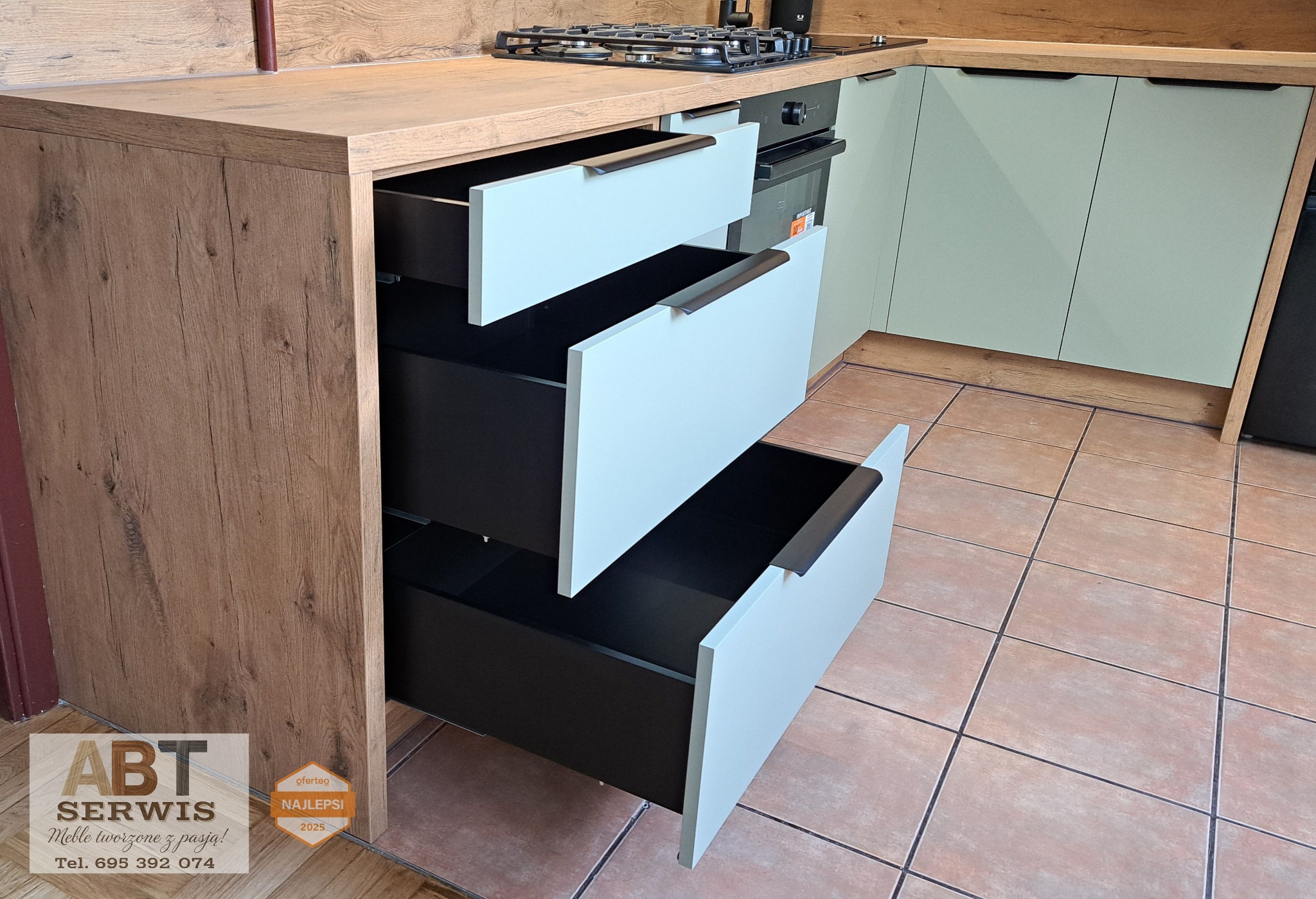 Nowoczesna kuchnia z otwartymi szufladami w kolorach drewna i bieli. Widoczny fragment płyty grzewczej i piekarnika. Ujęcie z niskiego kąta.