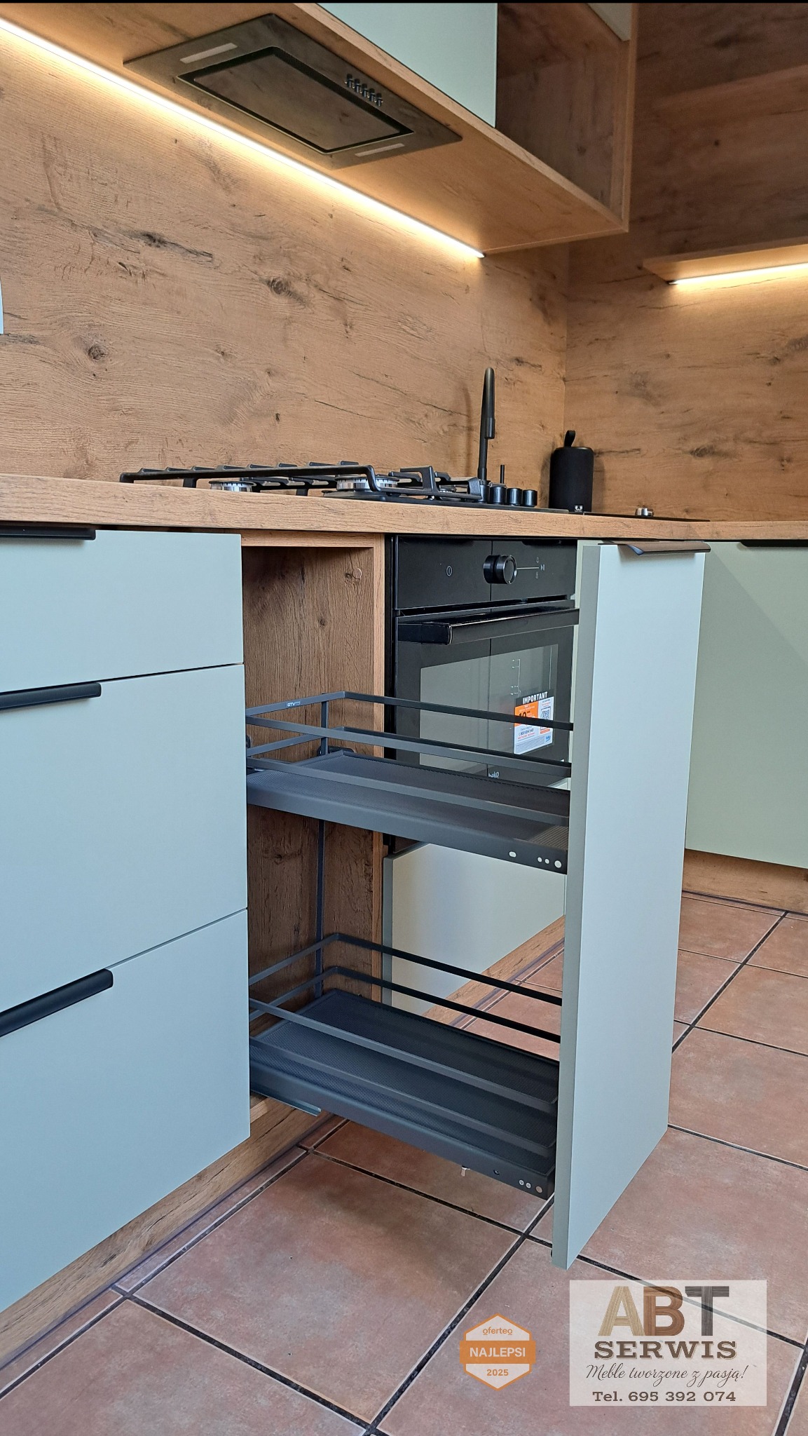 Nowoczesna kuchnia z wysuwanym koszem cargo, fronty w odcieniach szarości, drewnopodobny blat i okładzina ścienna, oświetlenie LED podszafkowe.