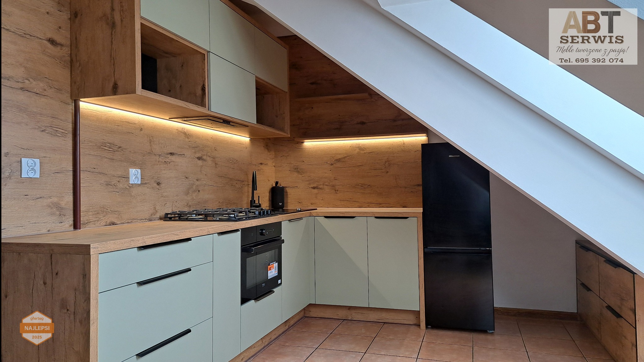 Nowoczesna kuchnia na poddaszu z drewnianymi akcentami i subtelnym oświetleniem LED. Jasne fronty szafek i czarny sprzęt AGD tworzą elegancki kontrast.