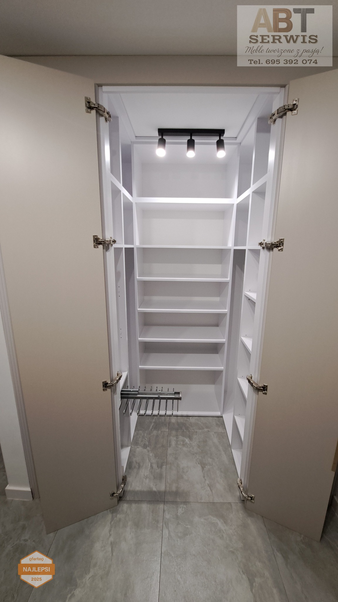 Otwarta szafa wnękowa z oświetleniem i wysuwanym wieszakiem na spodnie, wykonana na wymiar w Zgorzelcu. Białe półki i szare fronty drzwi.