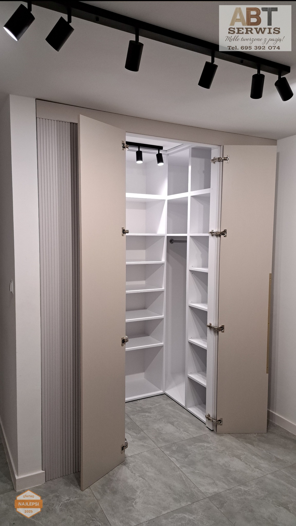 Otwarta, narożna szafa wnękowa z białymi półkami i beżowymi drzwiami, oświetlona punktowo. Widoczny fragment sufitu z reflektorami. Minimalistyczny design.