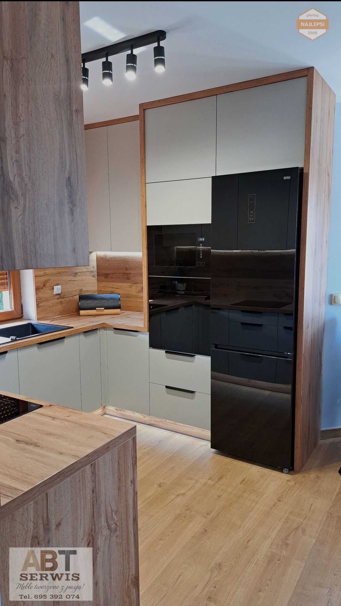 Nowoczesna kuchnia na wymiar z drewnianymi akcentami i czarnym sprzętem AGD. Widoczne oświetlenie punktowe i drewniana podłoga. Całość tworzy spójny i elegancki wygląd.