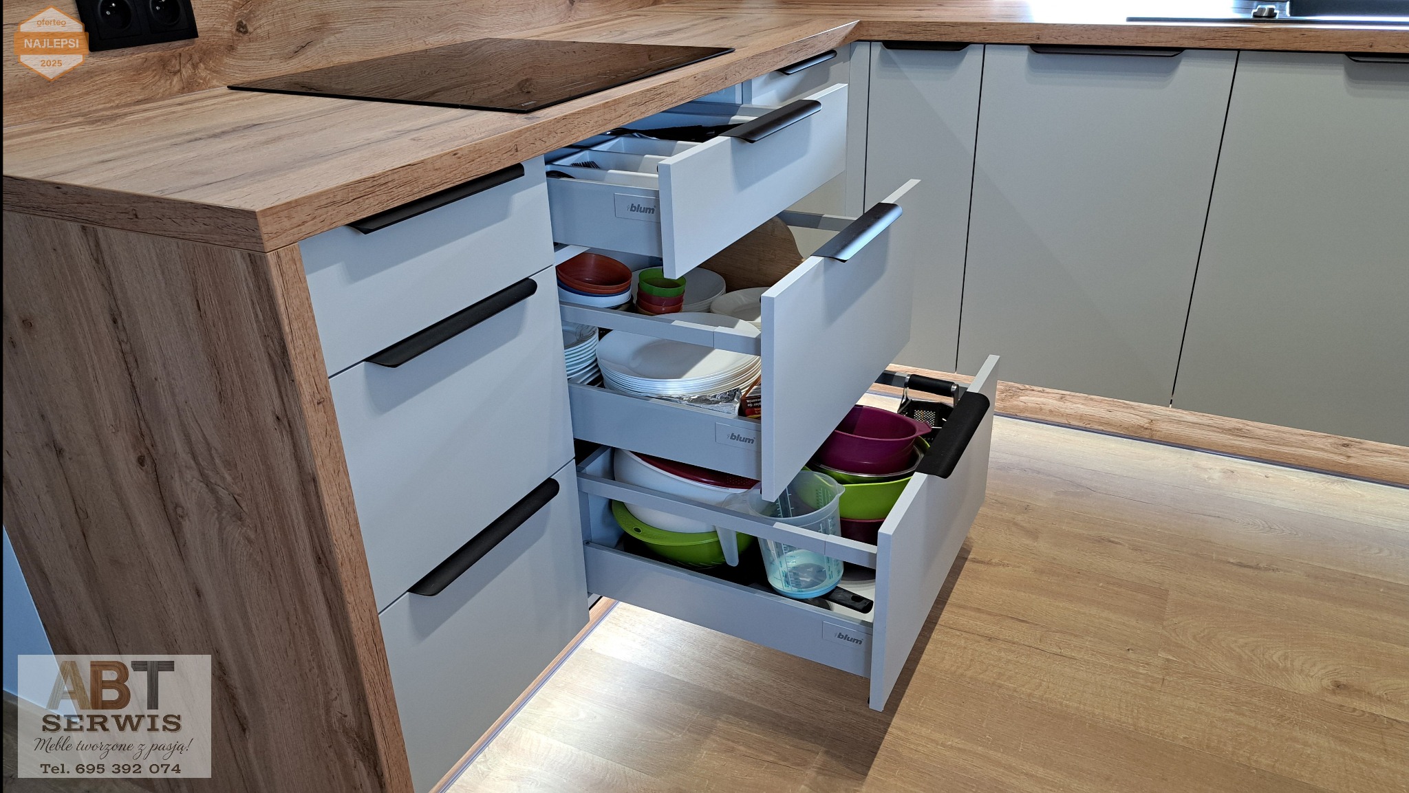 Nowoczesna kuchnia z szarymi frontami i drewnianym blatem. Wysuwane szuflady z pełnym wyposażeniem naczyń i akcesoriów kuchennych. Oświetlenie LED pod szafkami.