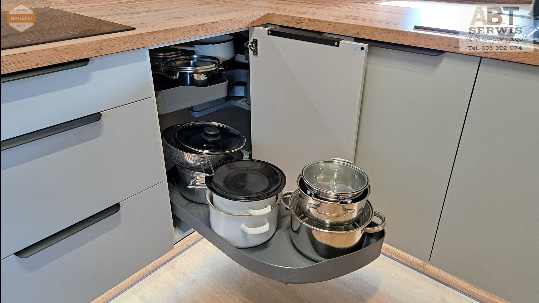 Szara kuchnia narożna z systemem cargo: garnki na wysuwanej półce. Drewniany blat i fronty bez uchwytów. Funkcjonalne rozwiązanie do przechowywania w kuchni.