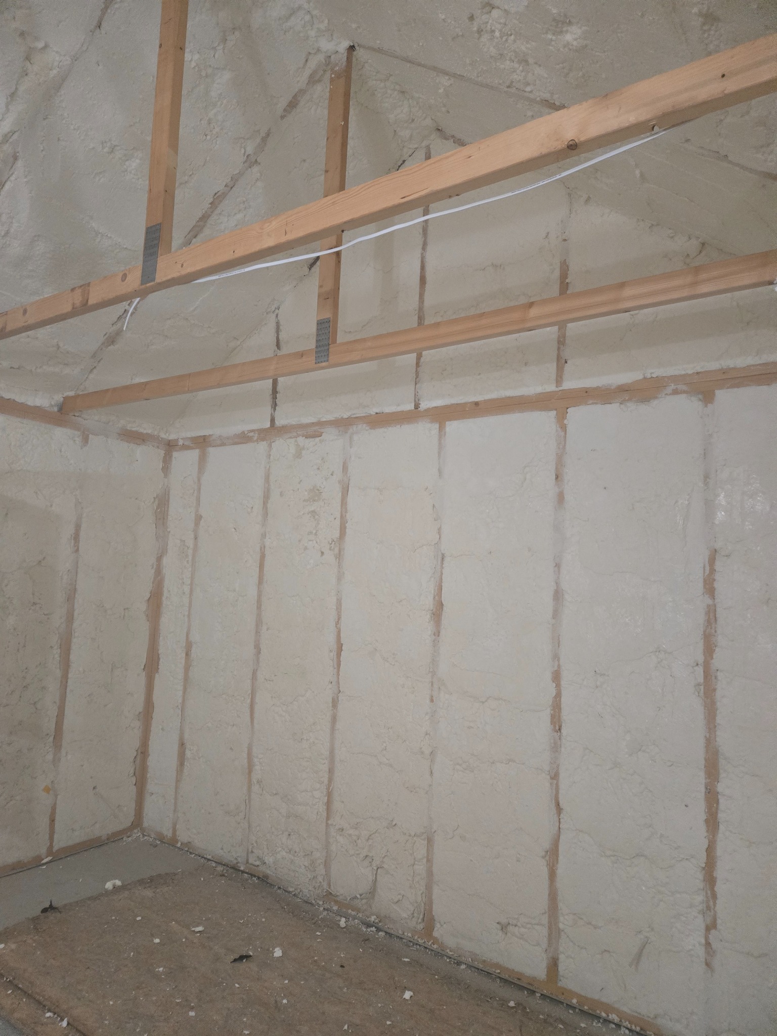 Poddasze po ociepleniu pianką PUR: widoczne drewniane elementy konstrukcyjne i równomiernie nałożona, jasna pianka izolacyjna na ścianach i suficie.